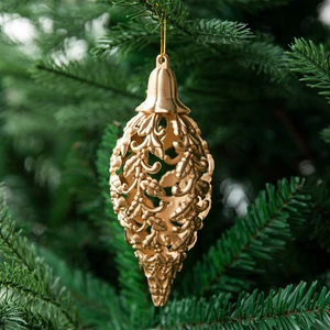 Golden hollowed teardrop Christmas ornament with leaf pattern hanging on a pine tree