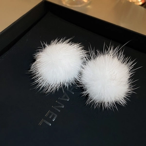 Close-up of white plush fur ball earrings on a black background for casual style