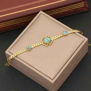 Golden flower bracelet with turquoise stones and flat chain on a beige jewelry box