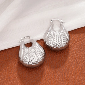 Détail macro de boucles d'oreilles coquillage argentées avec texture étoilée sur fond de soie