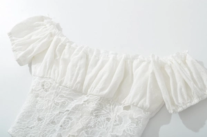 Detail of white off-the-shoulder top featuring elastic pleats and delicate lace embroidery