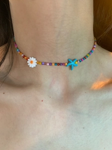 Close-up of a colorful beaded choker with white daisy flower and blue starfish charms