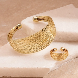 Close-up of gold geometric multilayer cuff bracelet and ring set on natural stone