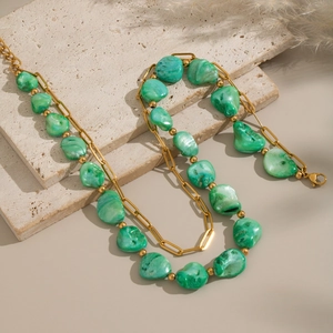 Close-up of golden chain necklace with irregular green stones on a stone pedestal