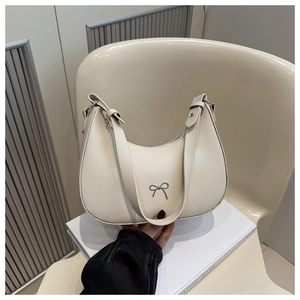 Detail of a creamy white crescent shoulder bag featuring a silver metal bow decoration