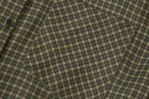 Detailed view of olive green plaid shirt featuring a chest pocket and black matte snap button