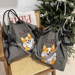 Close-up of grey nylon tote with corgi embroidery on a woven chair near a Christmas tree