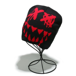 Dettaglio macro del berretto in maglia nera con volto di demone rosso e occhi a X