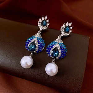 Macro detail of teardrop earrings with blue crystals and white pearl on leather surface
