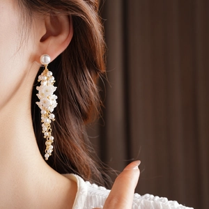Detail of floral tassel earrings with white pearls and gold chain on model
