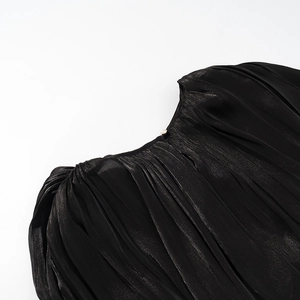 Détail du tissu noir plissé brillant avec une délicate fermeture à bouton perle
