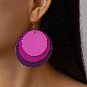 Detail view of tiered round wooden earrings with pink and purple gradients on a model