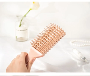 Detailed view of a pink hollow-out hairbrush held by hand against a clean backdrop