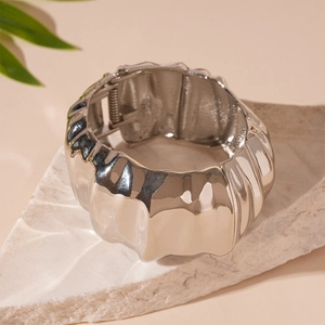 Detail of silver wavy metal cuff bracelet on white stone with green leaf accent
