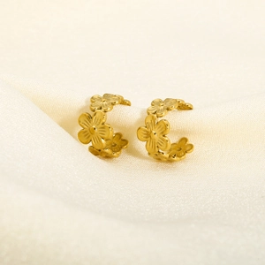 Detailed view of gold flower ear cuffs on soft beige fabric showing metallic texture