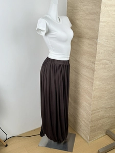 Detail view showing deep coffee pleated long skirt with elegant drape and flowing texture