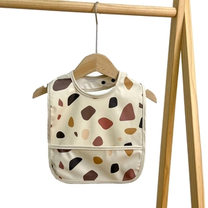 Waterproof baby bib with beige terrazzo pattern and food catcher on wooden hanger