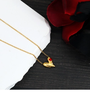 Détail d'un collier cœur plaqué or 18 carats avec pierre rouge sur fond de pierre