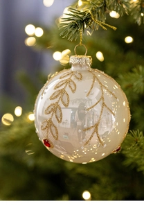 Detail of cream Christmas glass ball with gold glitter branch patterns on tree