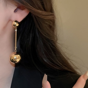 Close-up of elegant gold sphere drop earrings worn by a model in soft focus background