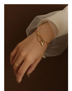 Close-up of 18K gold heart pendant bracelet and twisted ring worn by model
