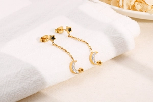 Detail of gold moon and star tassel earrings with rhinestones on a soft white background