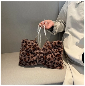 Detail of leopard print faux fur bow bag with elegant pearl beaded handle on a sofa