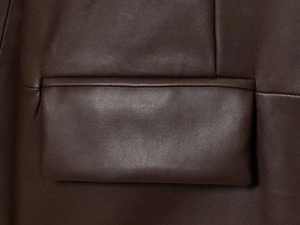 Close-up of deep brown leather jacket featuring a pocket detail and precise stitching