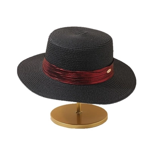 Elegant black straw boater hat with a burgundy ribbon on a minimalist gold stand