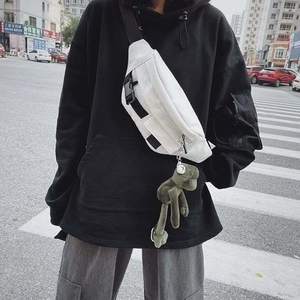 White canvas crossbody bag with black strap and green plush pendant street style view