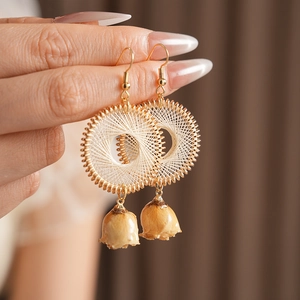 Close-up of golden woven earrings with white geometric patterns and small dried rosebuds