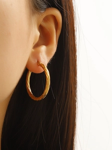Detailed close-up of golden twisted hoop earring with spiral texture on a female model