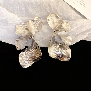 Close-up of large silver 3D floral earrings with intricate metallic petal textures
