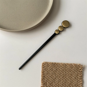Detail of minimalist black hair pin featuring three brushed gold circular metal accents