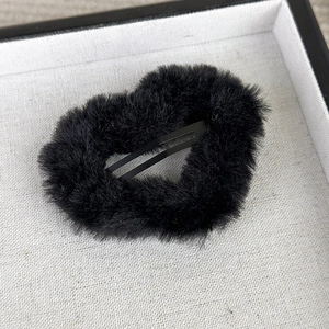 Detailed view of a black fuzzy plush heart hair clip on a minimalist jewelry tray