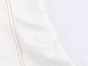 Détail du tissu denim blanc avec double couture marron contrastée et texture textile