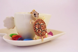 Detail shot of golden turtle keychain with brown rhinestones leaning on a heart cup