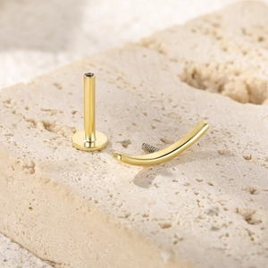 Macro view of a gold S925 silver butterfly labret stud on a textured stone surface