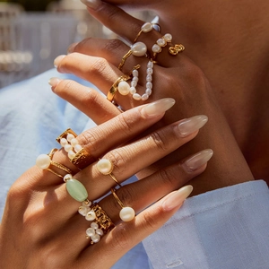 Detail of stacked gold rings with freshwater pearls and green gemstone on hand