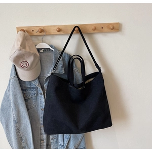 Detail of black canvas tote bag with shoulder strap hung on a wooden wall hook