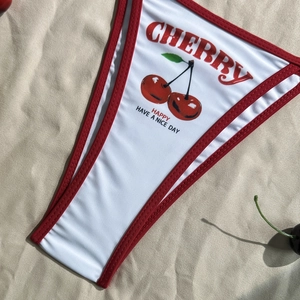 Detail of white bikini bottoms with red trim featuring cherry print and graphic text