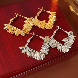 Close-up of gold and silver leaf square hoop earrings on a dark wood background