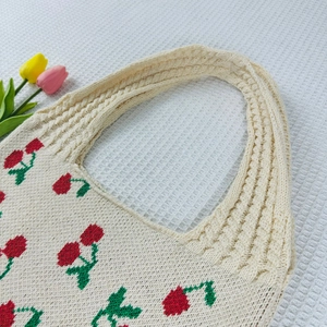 Detail of beige knit tote bag featuring crochet cherry pattern and woven shoulder strap