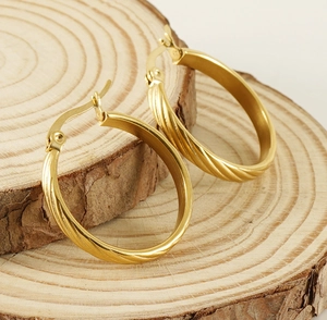 Detailed view of gold twisted hoop earrings placed on a rustic natural wood slice