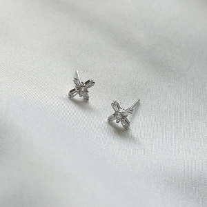 Detailed view of silver cross stud earrings with cubic zirconia on white silk