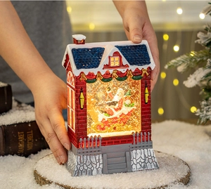 Close-up of a lit Christmas snow globe house with Santa and falling snow held in hand