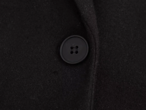 Detailed close-up of a black button on high-quality wool-like fabric of the coat