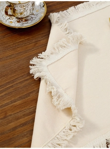 Close-up of cream boho placemat with fringe detail on wooden table with coffee cup
