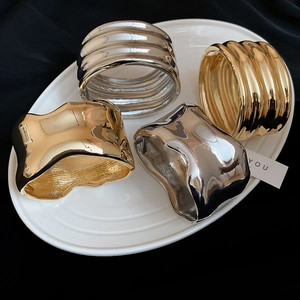 Polished gold and silver irregular cuff bracelets displayed on a white ceramic tray