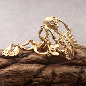 Golden gothic skeleton ring with sparkling diamond eye on textured dark wood background